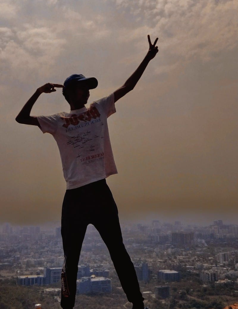 Ishaan Dalvi standing on mountain summit overlooking Pune skyline with victory gesture